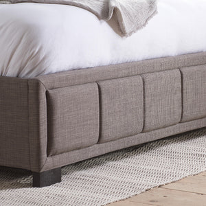 Gray upholstered bed with white bedding on a wooden floor.