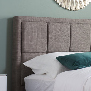 Gray upholstered headboard with white and teal pillows on a bed against a light green wall.