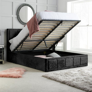 Black upholstered bed with storage compartments in a room with white walls and a window.