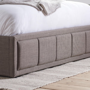 Gray upholstered bed with white bedding on a wooden floor.
