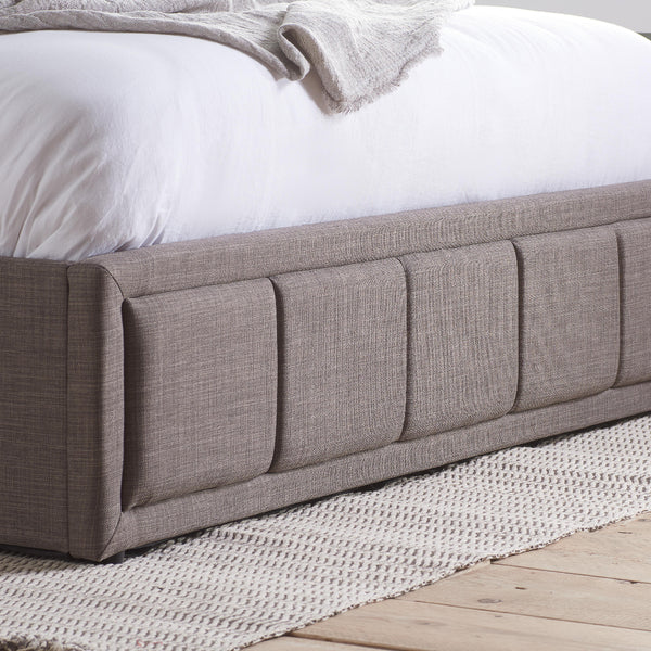 Gray upholstered bed with white bedding on a wooden floor.
