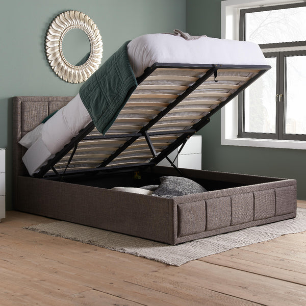 Brown upholstered bed with storage compartment open in a room with a mirror and window.
