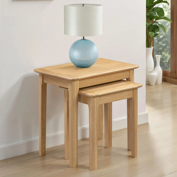 Two wooden nesting tables with a lamp on top in a room setting.