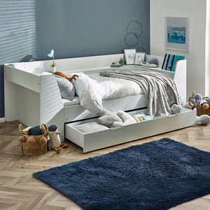 White bed with storage drawers in a room with a blue rug and toys.