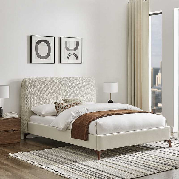 Beige upholstered bed in a modern bedroom with abstract art on the wall.