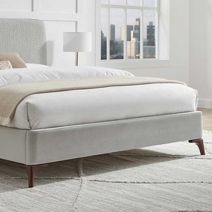 Modern bed with beige blanket and white bedding in a room with large windows.