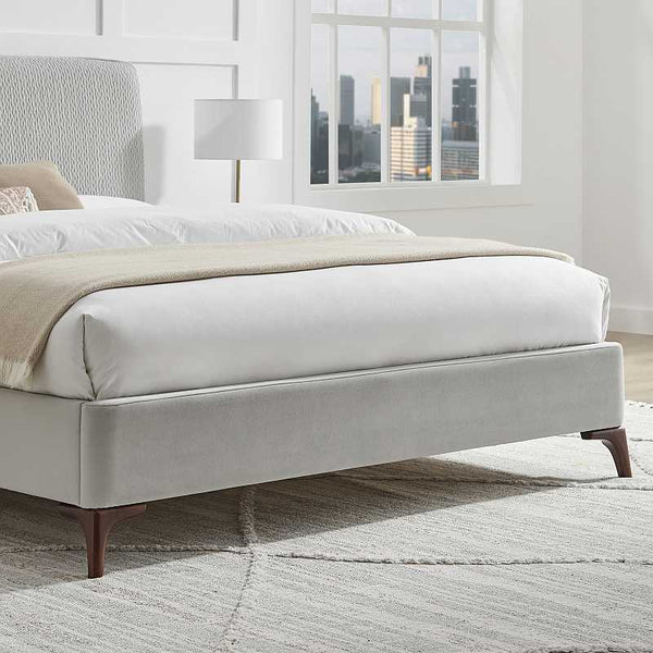 Modern bed with beige blanket and white bedding in a room with large windows.