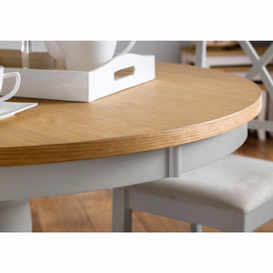 Round wooden table with a white base and a chair in a room setting.