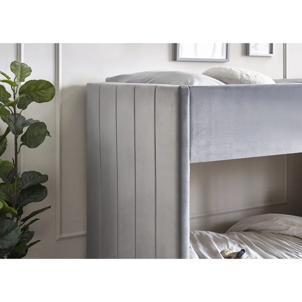 Bunk bed with gray headboard in a room with a plant and framed pictures on the wall.