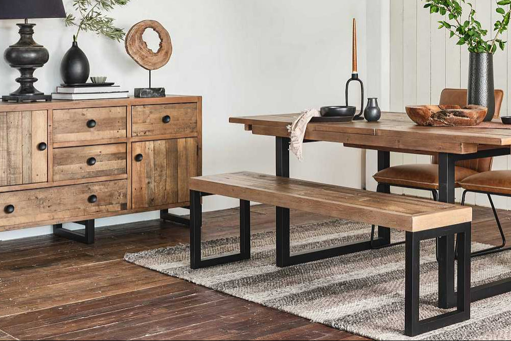 Dining room with wooden table, chairs, and bench on a striped rug.