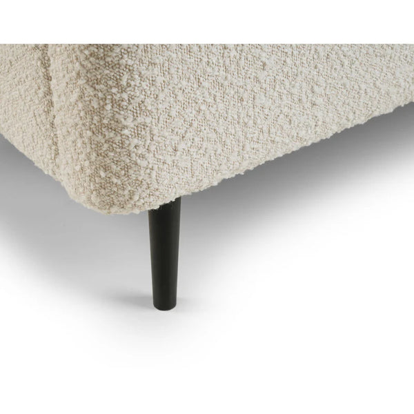 Close-up of a textured beige bed corner with a black leg on a white background