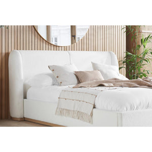 White upholstered bed with beige pillows and blanket in a room with wooden walls and a mirror.