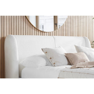 White upholstered bed with beige pillows against a wooden wall.
