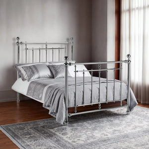 Silver metal bed with bedding in a room with wooden flooring and curtains.