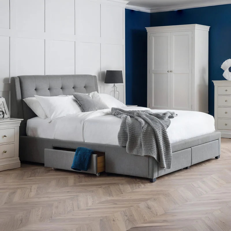Gray upholstered bed with white bedding and a gray blanket on a white background