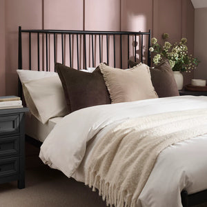 Neatly made bed with decorative pillows and a nightstand in a bedroom setting.