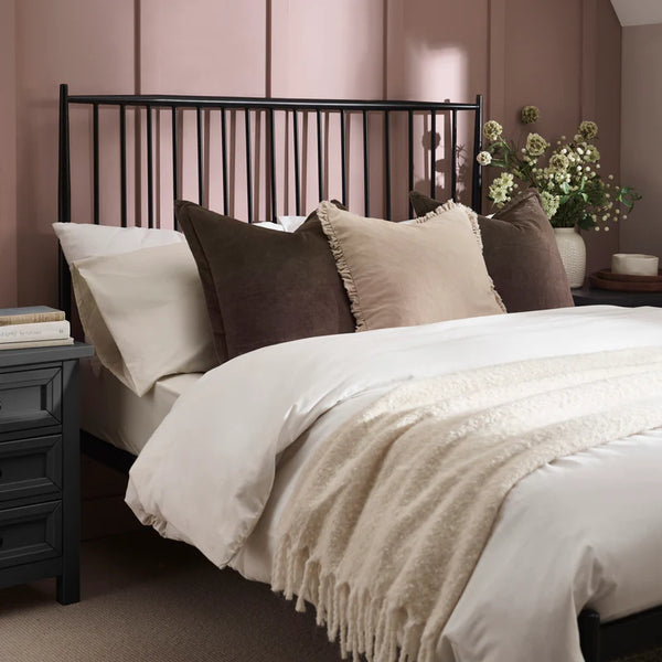 Neatly made bed with decorative pillows and a nightstand in a bedroom setting.