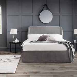 Gray upholstered bed in a modern bedroom with gray walls and wooden flooring.