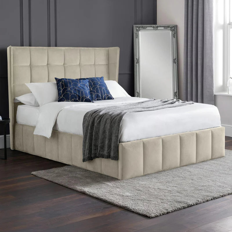 Cream upholstered bed with white bedding and a dark blue blanket on a white background