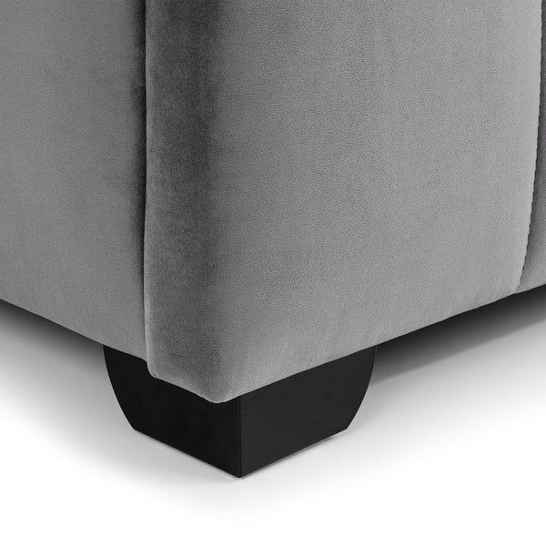 Gray upholstered corner of a bed with black legs on a white background