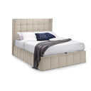 Cream upholstered bed with white bedding and a dark blue blanket on a white background
