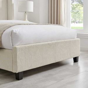 Beige upholstered bed frame in a bedroom setting with a lamp and window.