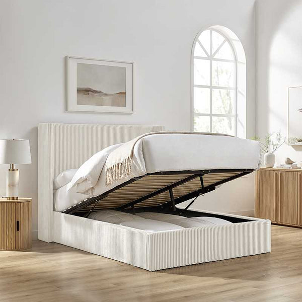 Beige upholstered bed with storage drawers in a bright bedroom setting.