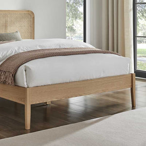 Wooden bed with white bedding and a brown throw blanket in a bright room.