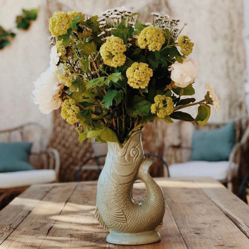Gluggle jug vase with a fish design holding a bouquet of yellow flowers on a wooden table.