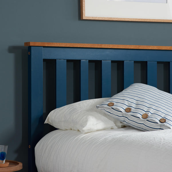 Blue wooden bed frame with white bedding and a striped pillow against a blue wall.