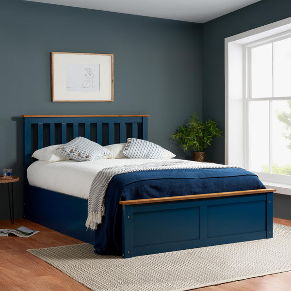 Blue bed with wooden accents in a bedroom with a window and plant.