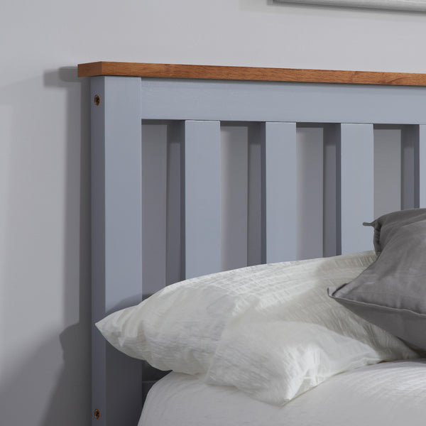 Gray wooden bed with white bedding and gray pillow against a plain wall