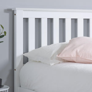 White wooden bed frame with pink pillow against a light gray wall