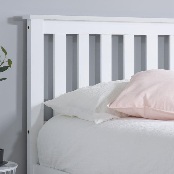 White wooden bed frame with pink pillow against a light gray wall