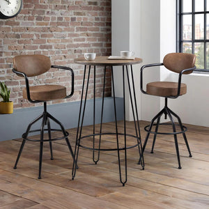 Two brown bar stools with black metal frames in front of a wooden table against a brick wall.