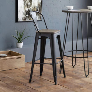 Bar stool with wooden seat and black metal frame in a room with a plant and wooden box.