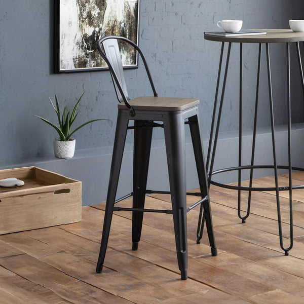 Bar stool with wooden seat and black metal frame in a room with a plant and wooden box.