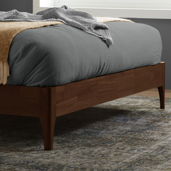 Wooden bed with gray bedding and a blanket in a room setting