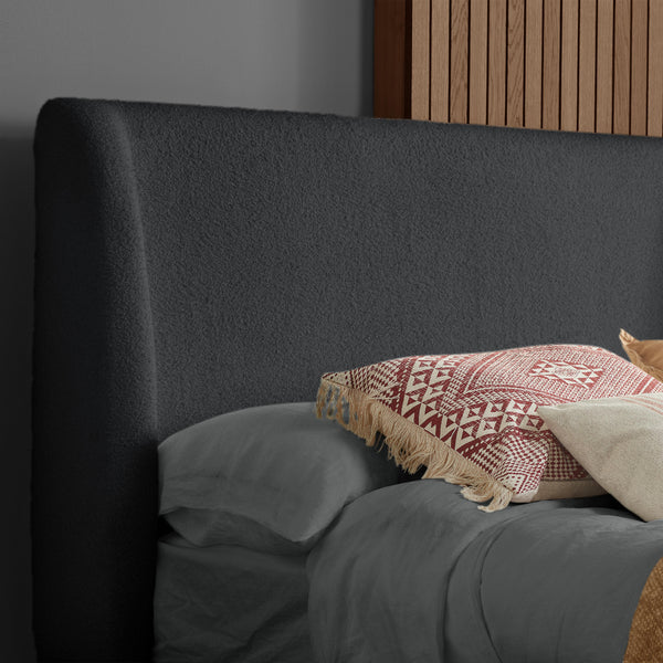 Gray upholstered headboard with pillows and a patterned blanket on a bed.