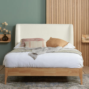 Wooden bed with white bedding and decorative pillows against a green wall.