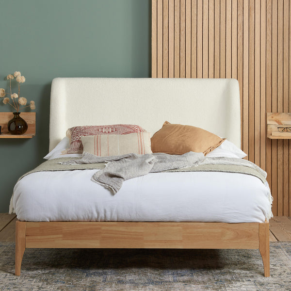 Wooden bed with white bedding and decorative pillows against a green wall.