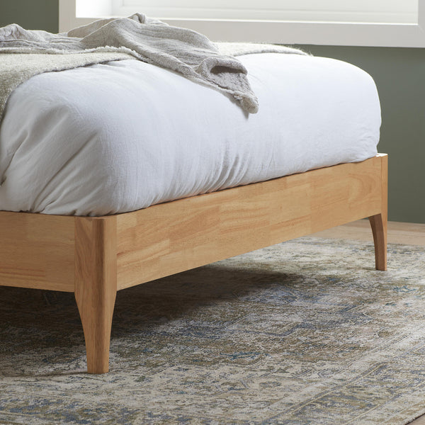 Wooden bed frame with white bedding and gray blanket on a patterned rug.