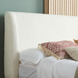 Close-up of a bed with white bedding and decorative pillows against a light blue wall.