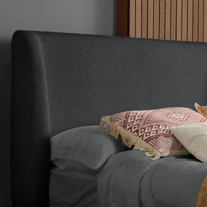 Gray upholstered headboard with patterned throw blanket and pillows on a bed.