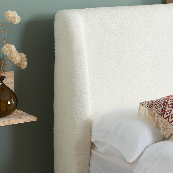 Close-up of a textured white headboard with a decorative pillow and vase on a shelf.