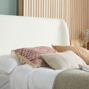White bed with patterned and solid pillows against a wooden headboard.