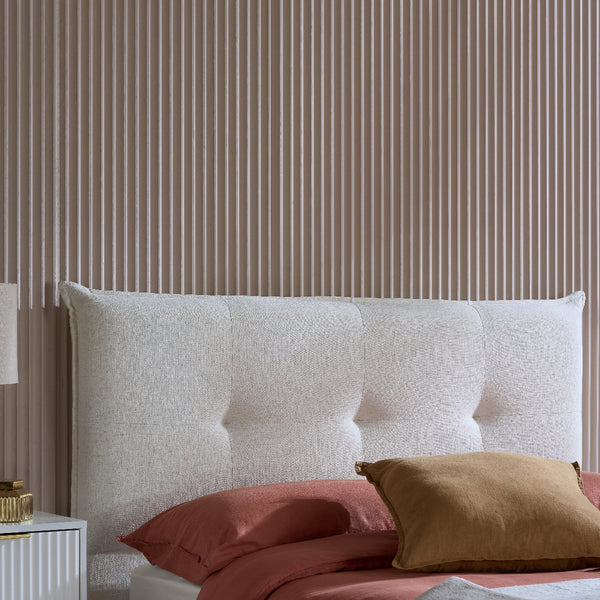 White upholstered headboard with red and brown pillows against a striped wall.
