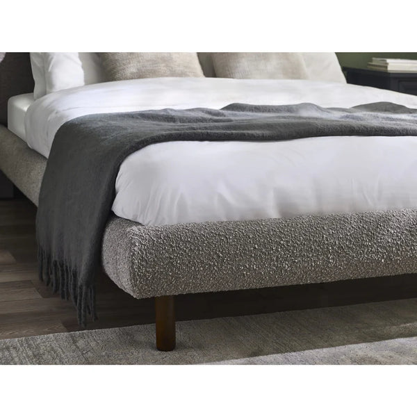 Gray upholstered bed with white mattress and gray blanket on a wooden floor.