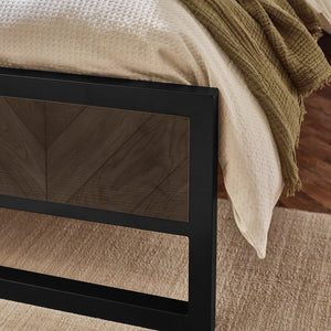 Close-up of a black metal bed frame with beige bedding and a green blanket.