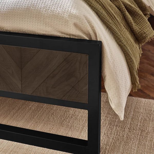 Close-up of a black metal bed frame with beige bedding and a green blanket.